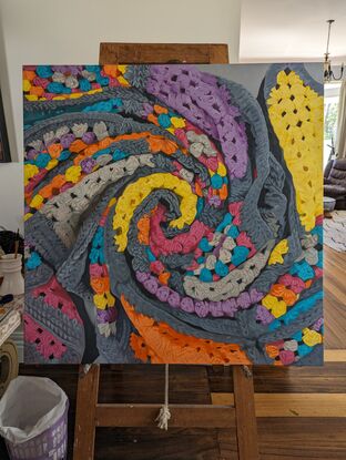 A crochet blanket folded into a swirl, that looks almost like an abstract painting with many colours, texture and depth.