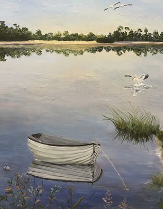 Pelicans fly overhead  and a boat is reflected in still water with reeds on the shore.