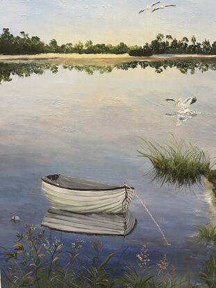 Pelicans fly overhead  and a boat is reflected in still water with reeds on the shore.