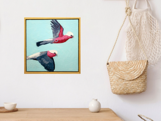 A textured oil painting of two pink galahs flying across the blue sky.