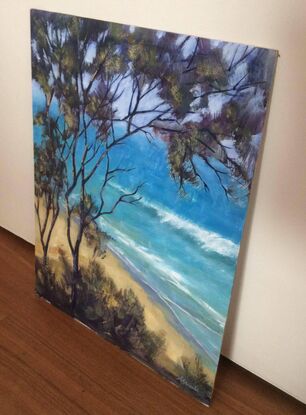 Looking through trees towards the azure water of an Australian beach, with gently waves rolling to shore.