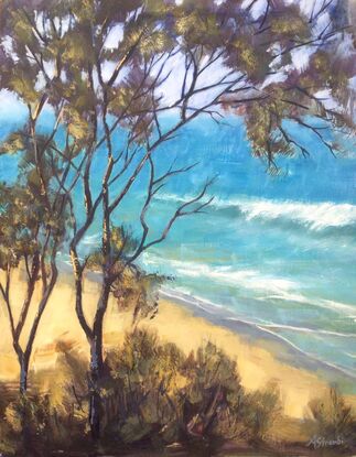 Looking through trees towards the azure water of an Australian beach, with gently waves rolling to shore.