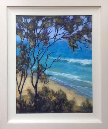 Looking through trees towards the azure water of an Australian beach, with gently waves rolling to shore.