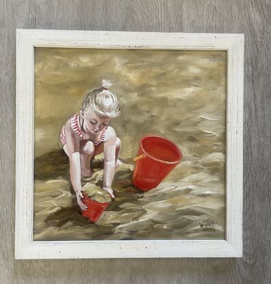 A young blued girl in red and white striped bathers crouches in golden sand playing with two red buckets. Framed in lined white wood.