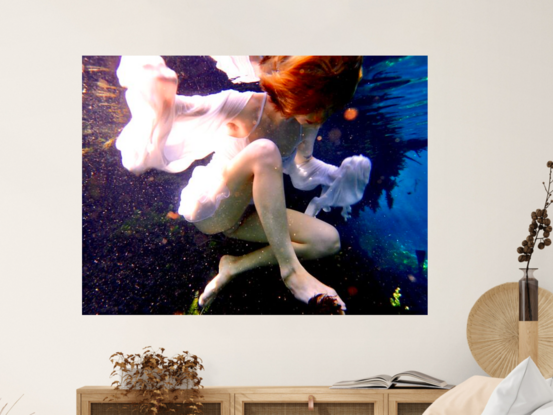 Young woman underwater showing reflections of her white dress in the swirling water whilst swimming.