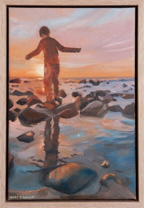 Boy stepping across stones at the beach at sunset.