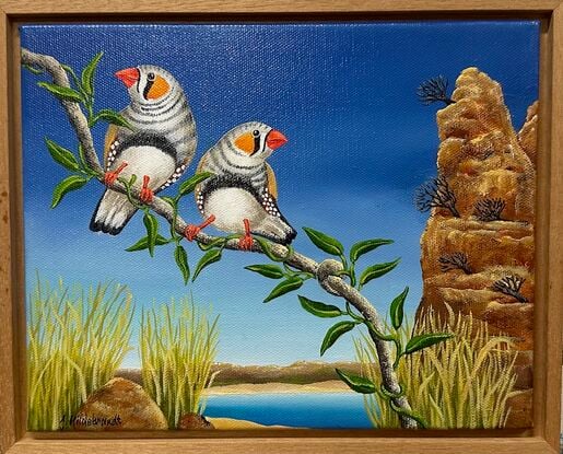 In the foreground are 2 zebra finches on a single branch. The background depicts a waterhole with high barren rocks and grass. It is all set to a background of a dark blue sky.