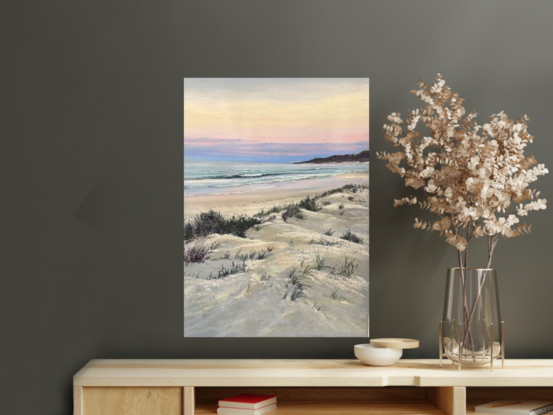 Headland with a bright sunny sky aqua water  hues of pink and yellow in the sky and soft sand dunes in the foreground 