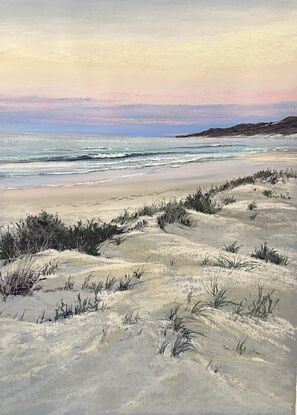 Headland with a bright sunny sky aqua water  hues of pink and yellow in the sky and soft sand dunes in the foreground 