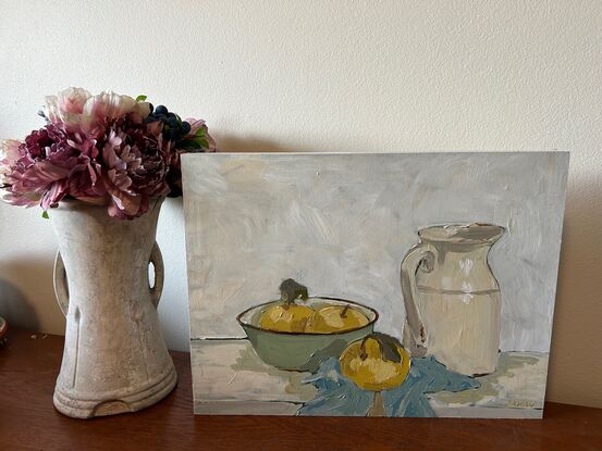 A still life scene with light green enamel bowl with light yellow nashi pears in it. To the right is an old ceramic cream coloured milk jug and they both sit on a light blue tea towel crumpled underneath. The background is white