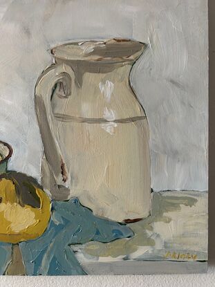 A still life scene with light green enamel bowl with light yellow nashi pears in it. To the right is an old ceramic cream coloured milk jug and they both sit on a light blue tea towel crumpled underneath. The background is white