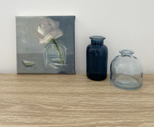 A single cream rose in a glass vase on the bench.