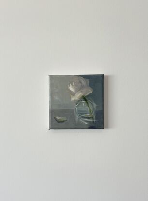 A single cream rose in a glass vase on the bench.