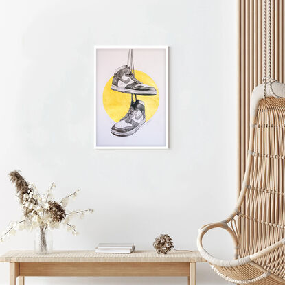 A graphite balck and white drawing of two Nike Dunk high top shoes hanging from their shoe laces from height reminiscent of telegraph wires. Behind the shoes is a gold metallic halo. 