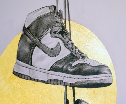 A graphite balck and white drawing of two Nike Dunk high top shoes hanging from their shoe laces from height reminiscent of telegraph wires. Behind the shoes is a gold metallic halo. 