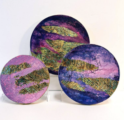 three circular abstract paintings in shades of pink and purple with elements of variegated gold