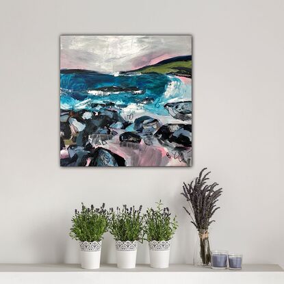 A coastal scene in pinks, blues and greys, with rocks  in the foreground, a blue ocean, a green headland and calm sky above. 