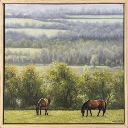 A framed oil painting of two horses grazy in a field with rain-swept, misty fields in the distance.