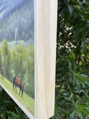 A framed oil painting of two horses grazy in a field with rain-swept, misty fields in the distance.