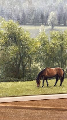 A framed oil painting of two horses grazy in a field with rain-swept, misty fields in the distance.