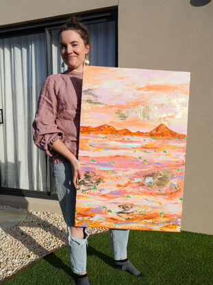 Pink and gold desert landscape with distant ranges in orange and an aerial type view of tiny green trees on a pink and pastel and gold embellished land. 