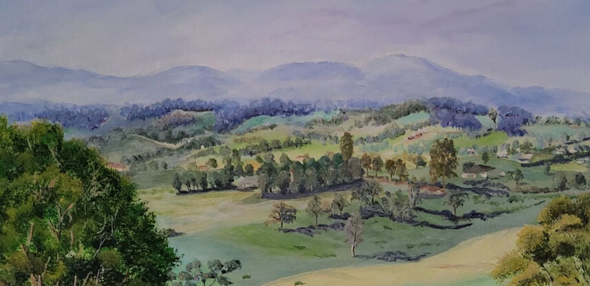 a panoramic view to the misty mountain ranges in the distance and the rolling hills of Bega Valley, with homes scattered around, surrounded by grasses, shrubs and trees with a working farm in the foreground and tall grasses and a hint of a fence in front, all framed by two large gum trees on either side of the artwork