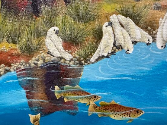 Barramundi swim in the waterhole while a flock of birds have gathered for a drink. A scene in the outback of Australia with overpowering red rocks in the foreground and boab trees at a distance.