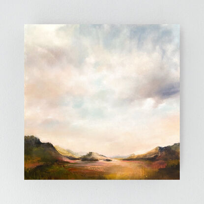 Softly lit sky, glowing peach and soft grey, brighten the rolling hills and open planes of the landscape below.