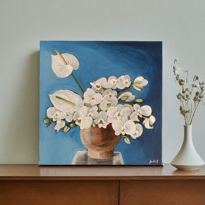 This painting features a vibrant still life of white orchids is set off against a rich blue background. The central focus is a collection of white orchids, their delicate petals contrasting beautifully with the darker hue. A few white Anthurium flowers add a touch of drama with their unique shape. The flowers are arranged in a simple, earthenware vase, further emphasizing their natural beauty. The overall composition is balanced and harmonious, creating a sense of tranquility and elegance.