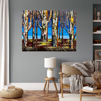 Several colourful gum tree trunks, a Kookaburra sitting in the tree with some leaf litter and twigs a lovely deep maroon with pops of green fading light blue upward to a bright blue sky 