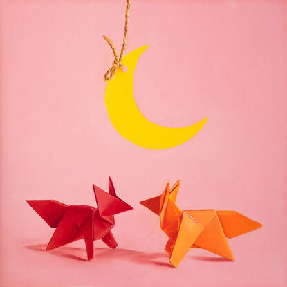 two origami foxes meeting under a hanging paper moon. the mood is fun and playful