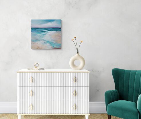 Gentle waves roll onto a sandy beach under a sky filled with cloud cover, creating a serene and calming scene. The hues of blue and green blend harmoniously, portraying the natural beauty of the coastal landscape. There are multiple layers of acrylic paint that gives the piece nuance, depth, and interest. The side edges are painted black and it is wired ready to hang. A clear UV protective finish coat finish the piece.