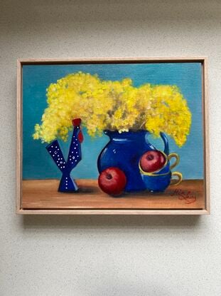 Wattle in a blue glass vase with apples and decor. 