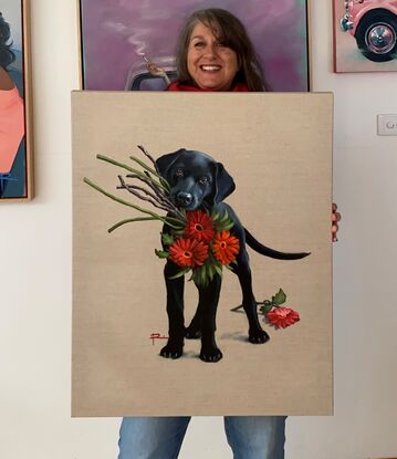 A black labrador puppy holding a bunch of red gerberas