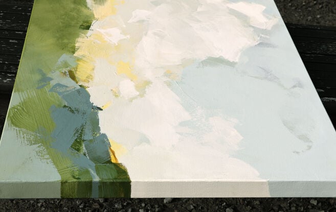 Loose abstract white clouds on a blue sky with touches of yellow  above a green and blue landscape.