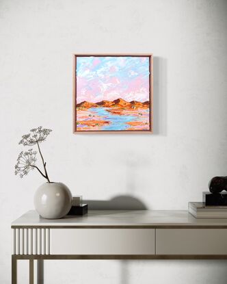 Pink and blue sky with peach toned ranges, tiny trees and a water way through the outback. 