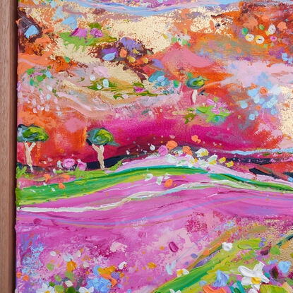 Foreground of wildflowers in a variety of colours in a hilly landscape of pink green and orange with flying birds overhead. 