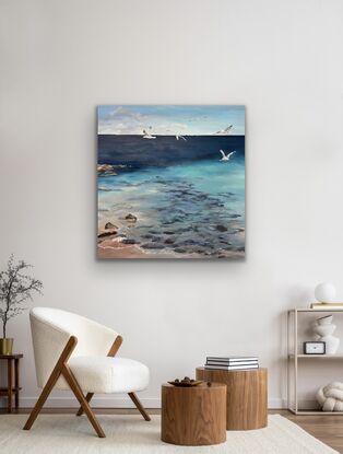 Seagulls fly over shallow water and rocks at the beach ona sunny day.