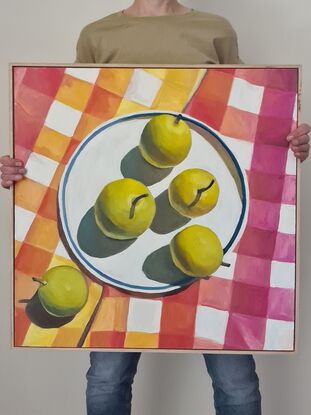 Looking down onto a plate of light green nashi pears sitting on a brightly checked oink, orange and yellow tablecloth.