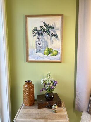 Stripy leaved plant cuttings in a glass bottle on a white tablecloth with 3 green pears alongside. 