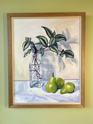 Stripy leaved plant cuttings in a glass bottle on a white tablecloth with 3 green pears alongside. 