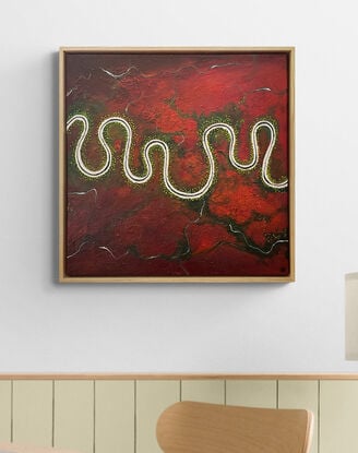 A vibrant and textured aerial landscape titled 'The Red Land of Wonder'. The painting features a vivid red expanse with a river meandering horizontally across the canvas. Dark green trees are dotted along the river.