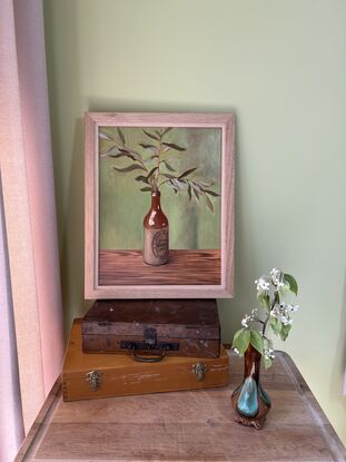 A vintage cream and brown stoneware bottle holding a spray of olive leaves. 