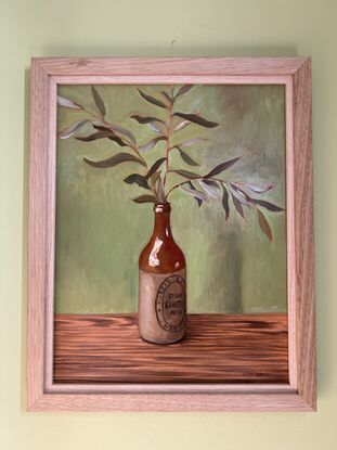 A vintage cream and brown stoneware bottle holding a spray of olive leaves. 