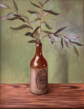 A vintage cream and brown stoneware bottle holding a spray of olive leaves. 