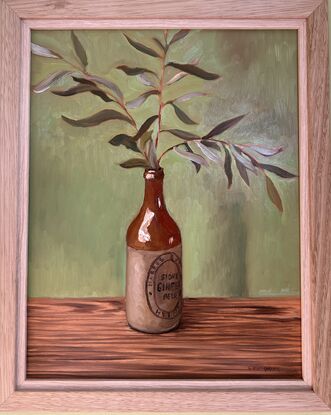 A vintage cream and brown stoneware bottle holding a spray of olive leaves. 