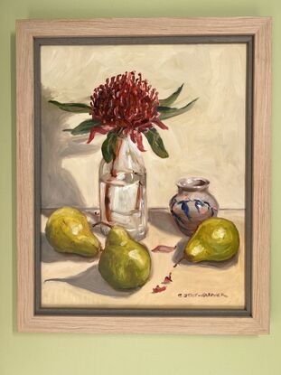 A red Waratah in a glass bottle surrounded by three pears and a small vase with blue and pink details