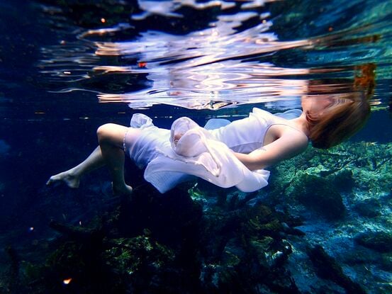 Young woman floating on the surface of the water  in a white dress - capturing beautiful reflections of light.