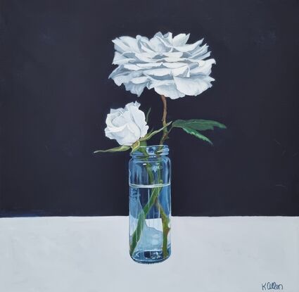 Two white roses in a marrow glass jar on a background split in two horizontally with a dark blue on the top and a pale grey white on the bottom. 