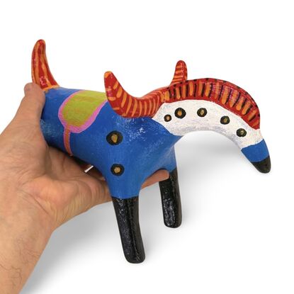 The Horned Wanderer sculpture features a bold blue body with vibrant red, curved horns and black legs, accented by colorful patterns and dotted details. 